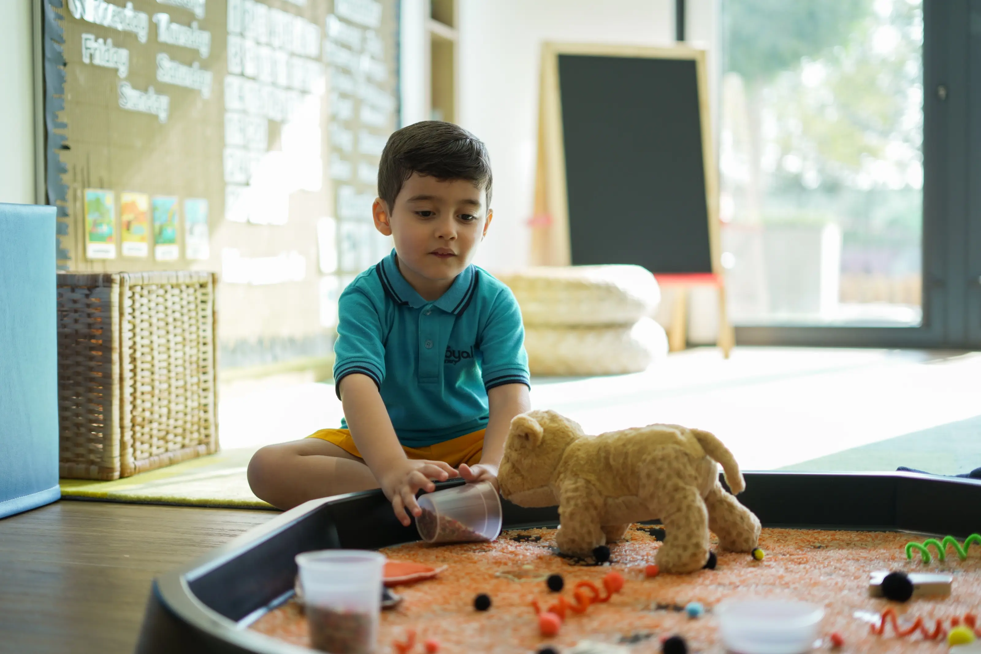 A child exploring a lentil sensory tray with a toy lion in window light