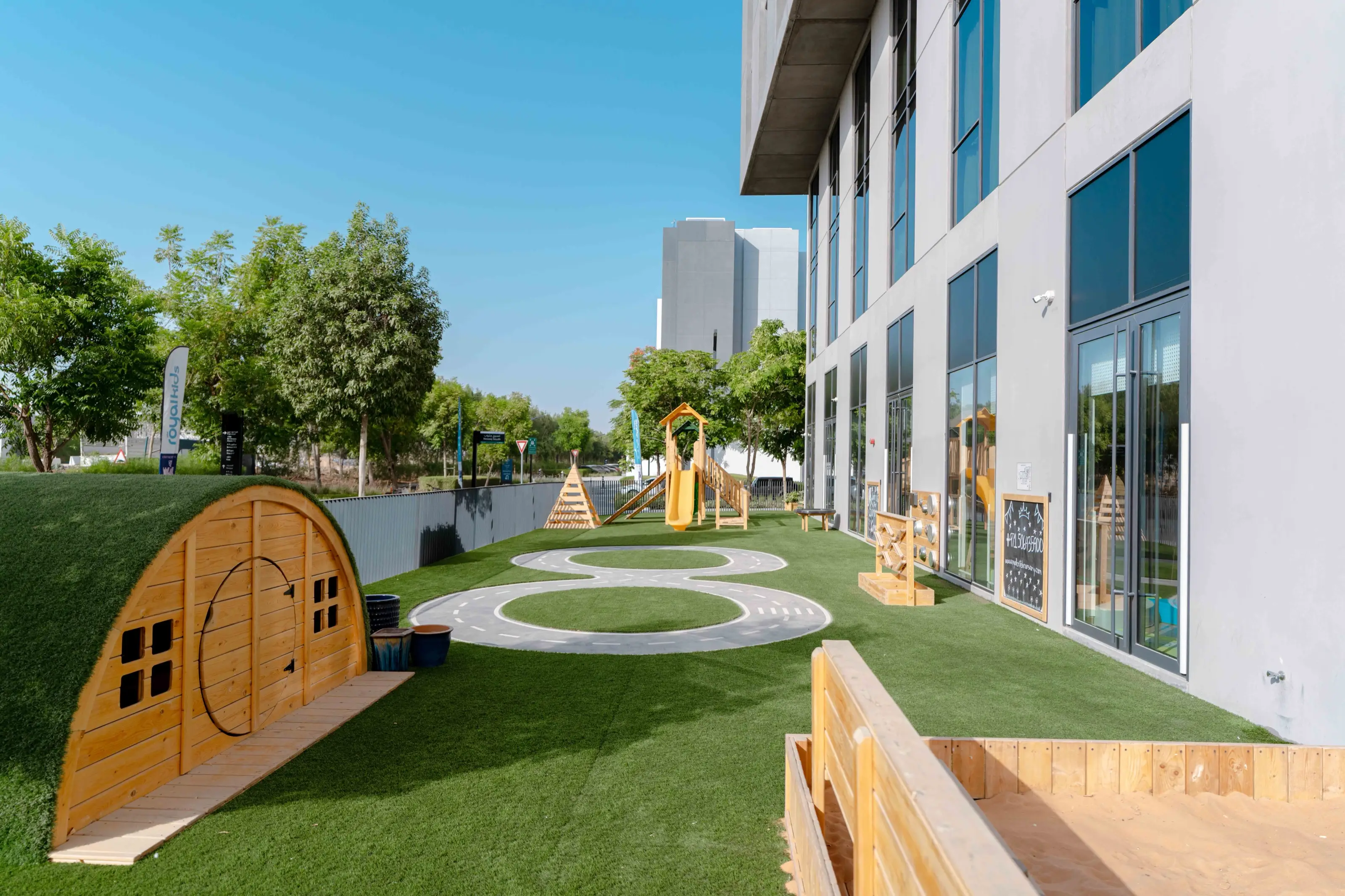 The Royal Kids Nursery courtyard with its play structure and lawn under a clear sky