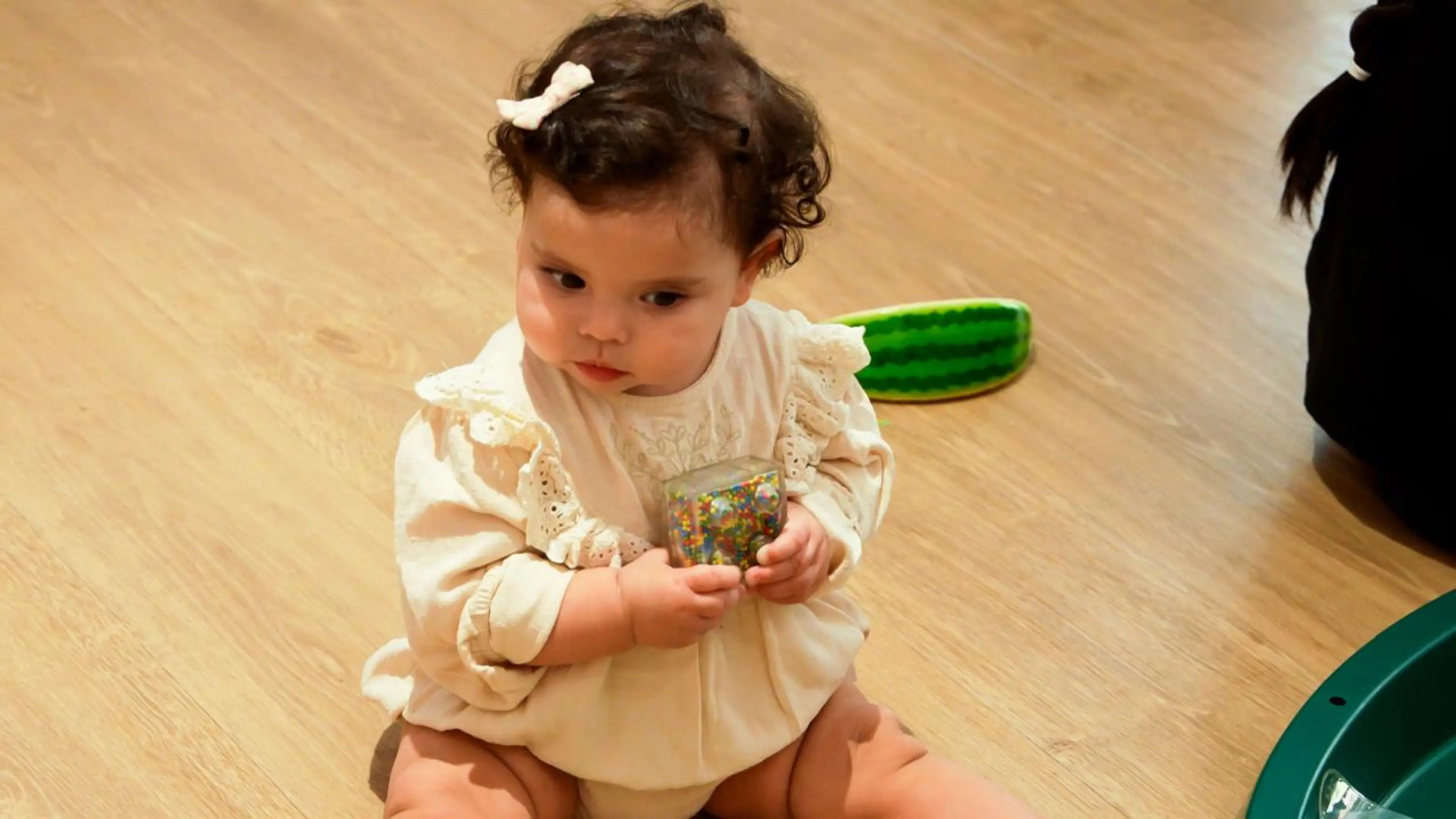 A baby in Pearl Class holding a sensory bottle on the classroom floor