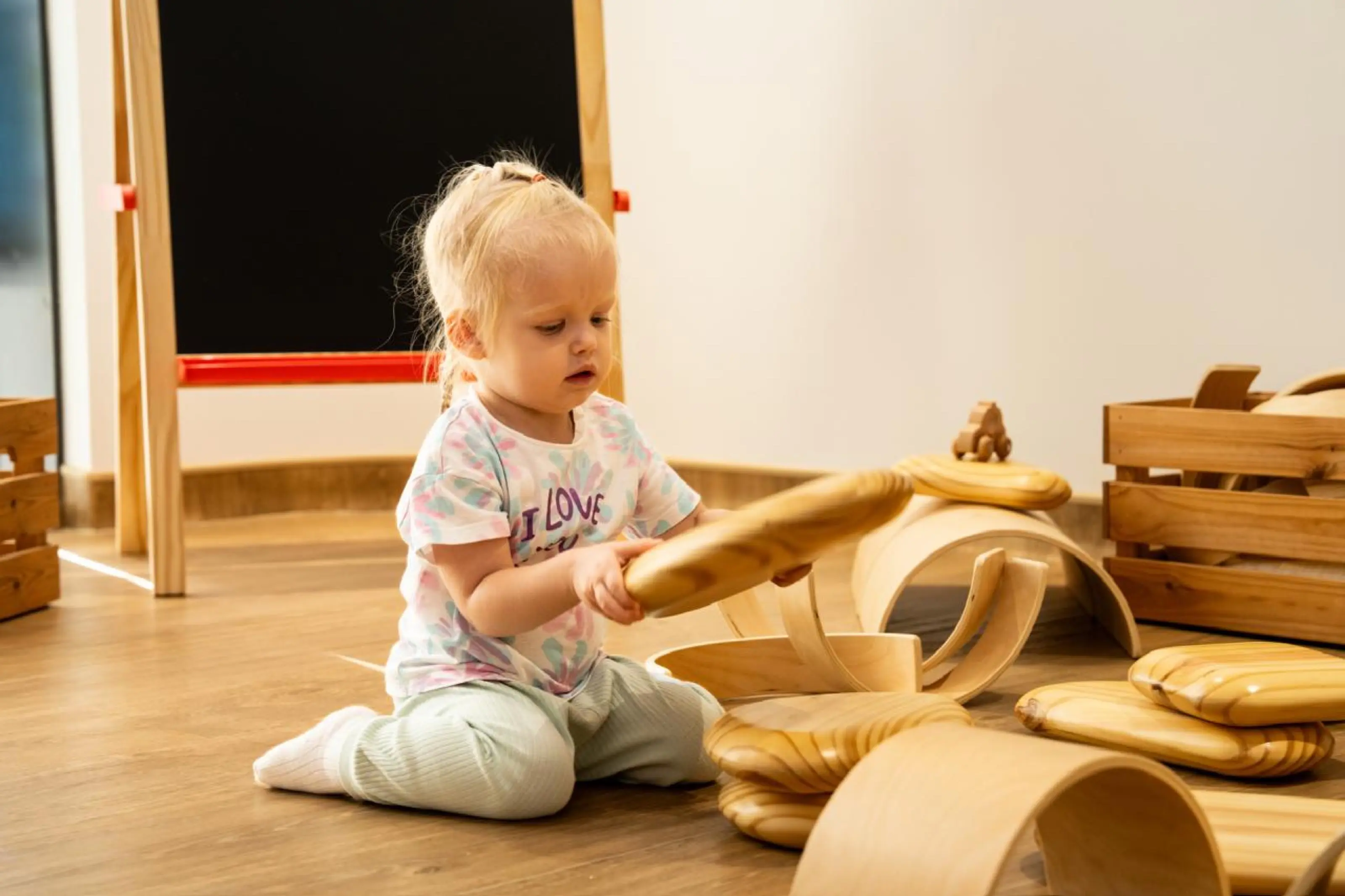 A toddler in Ruby Class building with large wooden blocks on the classroom floor
